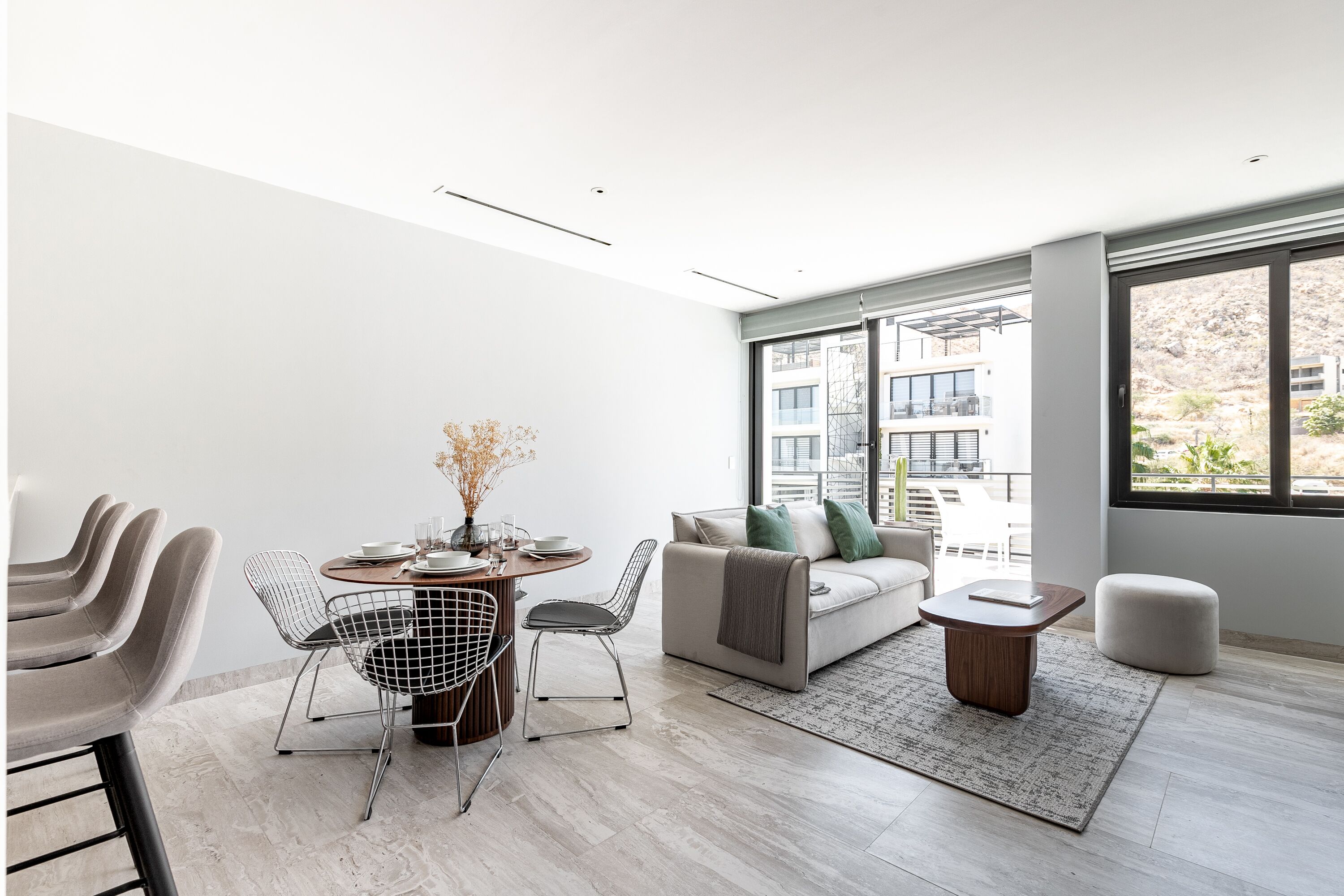 A modern living room with a dining area, large windows, and a view of buildings.