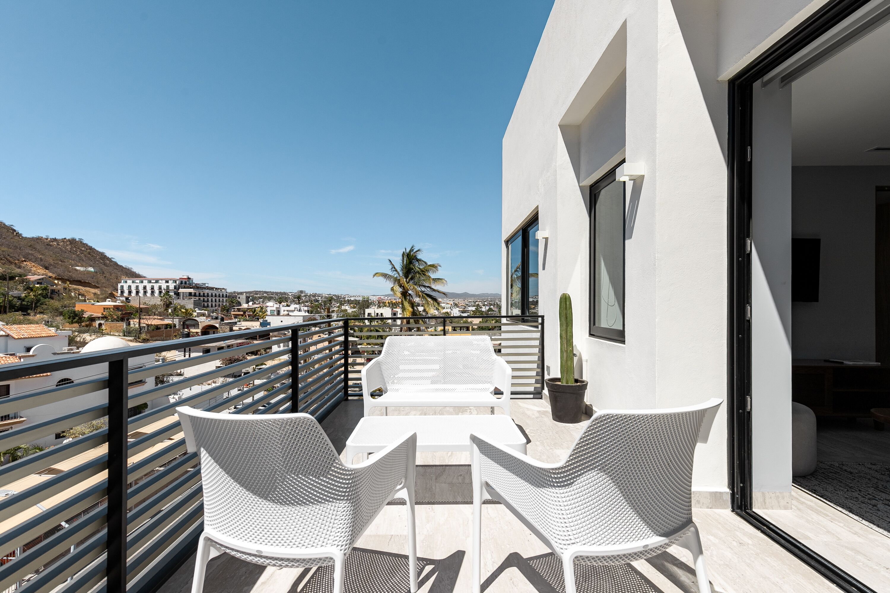 A balcony with white wicker furniture, a potted cactus, and a view of the cityscape.