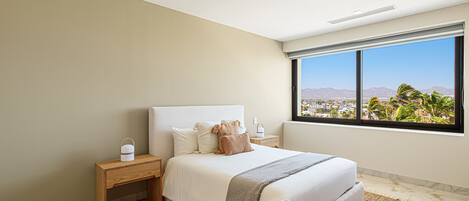 A bedroom with a large bed, a nightstand, a bedside table, and a window with a city view.