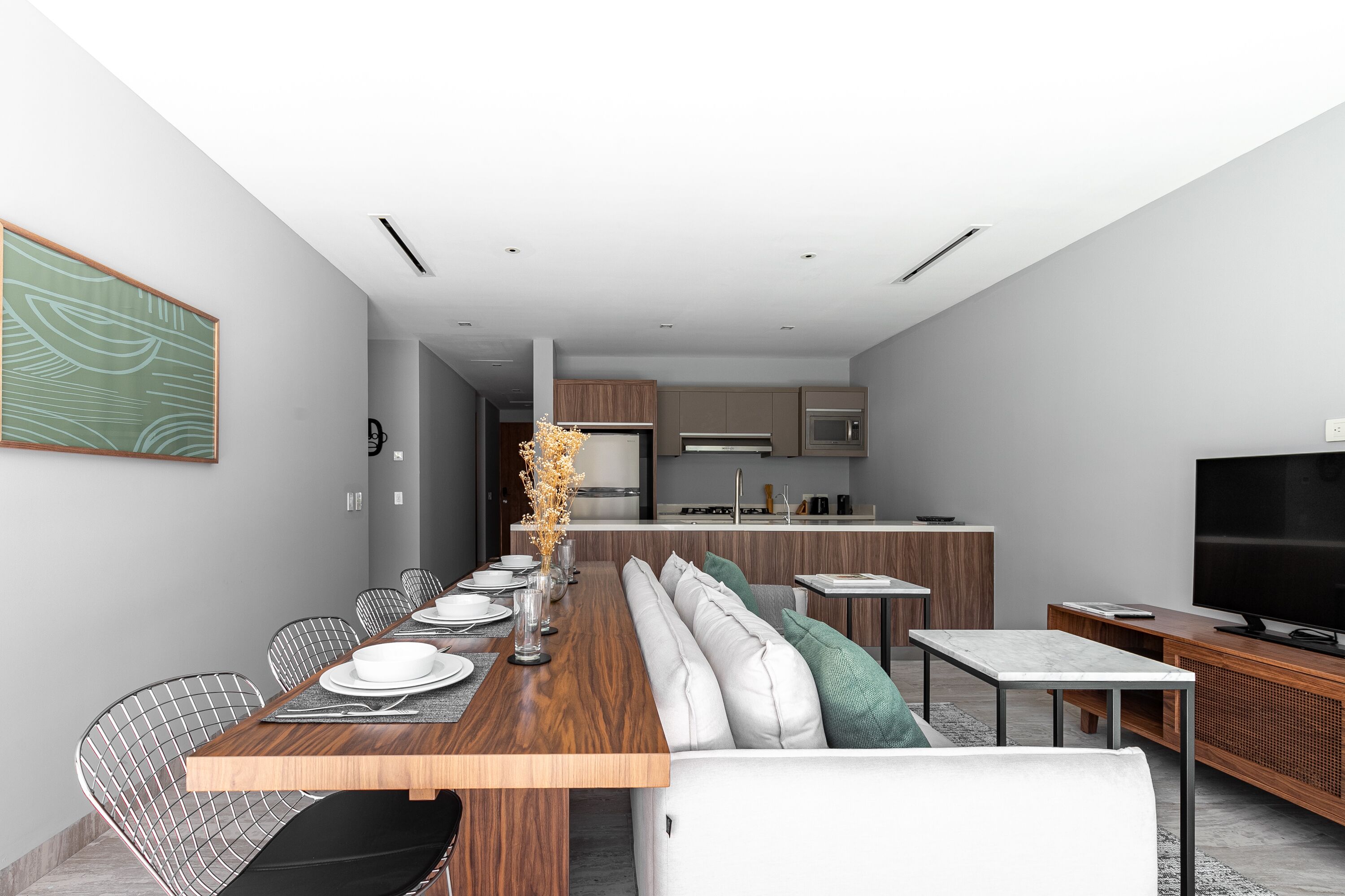 A modern living room with a dining area, a kitchen in the background, and a large flat-screen TV.