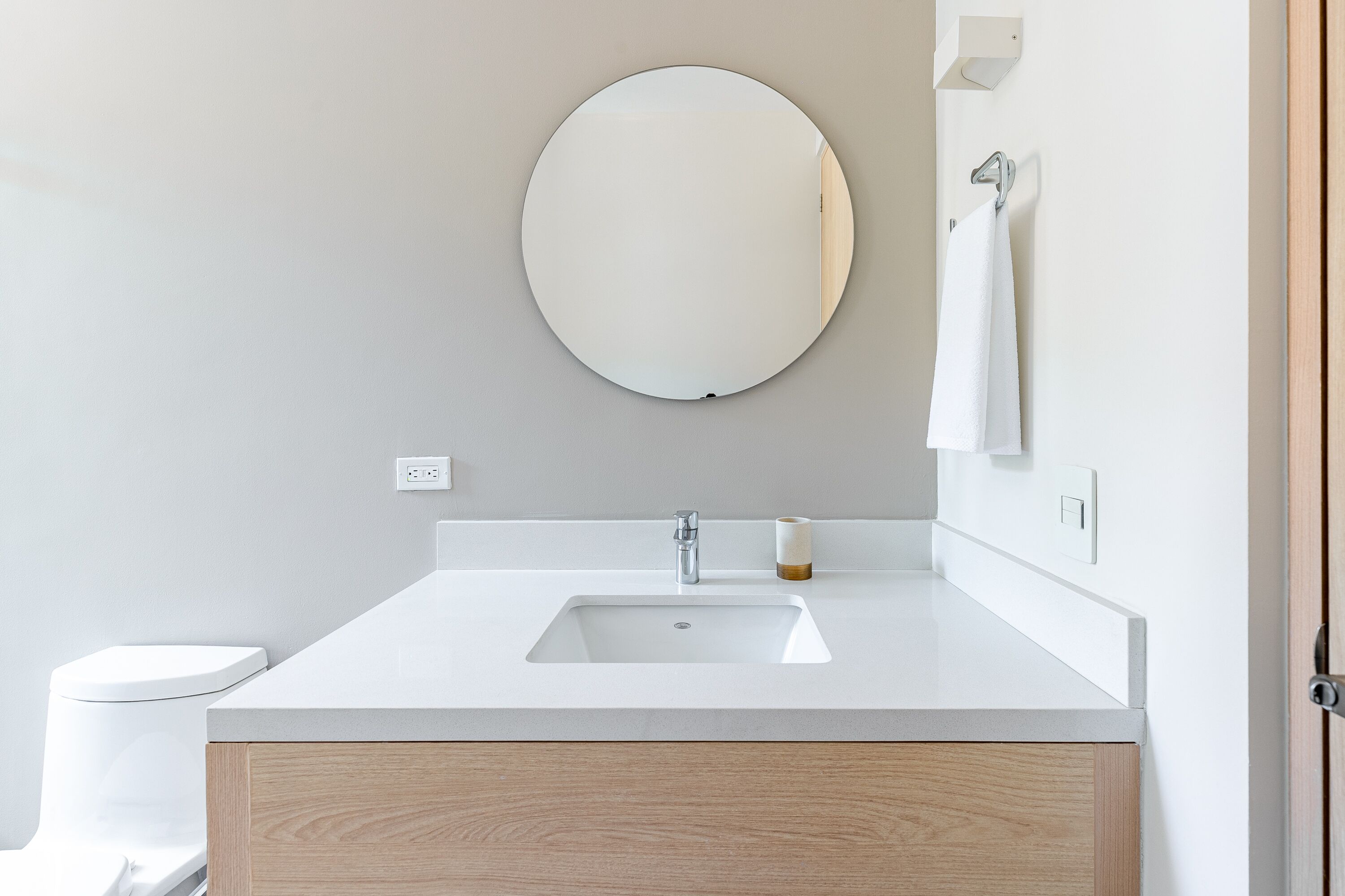A modern bathroom with a white sink, a round mirror, and a wooden vanity.
