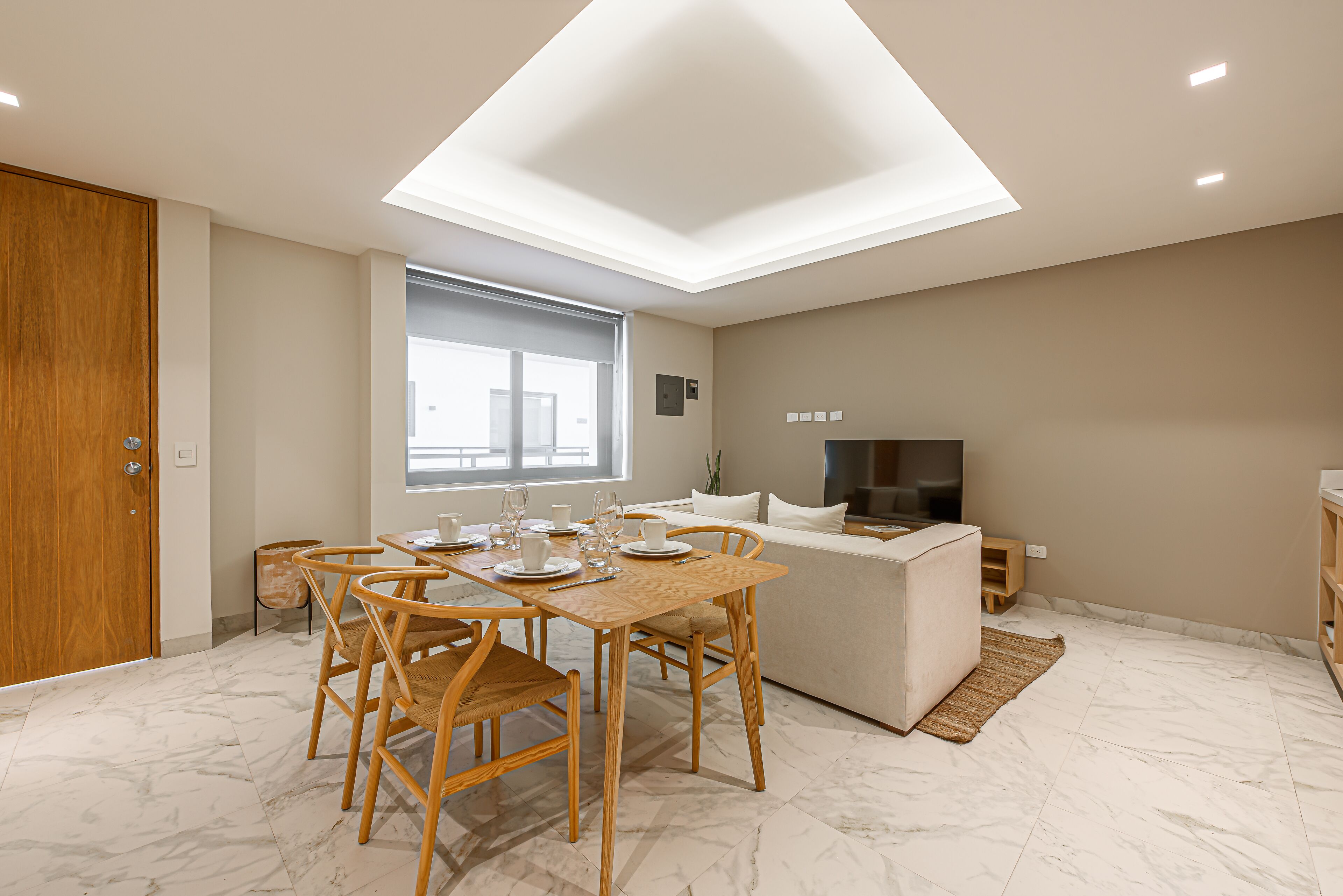 A modern kitchen with a dining area, featuring a wooden table and chairs, a built-in oven, and a large window.