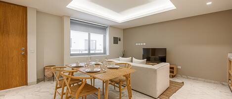 A modern kitchen with a dining area, featuring a wooden table and chairs, a built-in oven, and a large window.