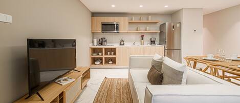 A modern, compact living space with a flat-screen TV, wooden furniture, a kitchen with a microwave, and a dining area.