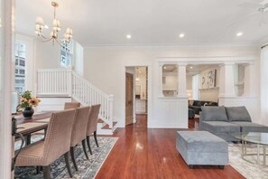 A spacious living area with a wooden floor, a dining table with chairs, a gray sofa, and a glass coffee table.