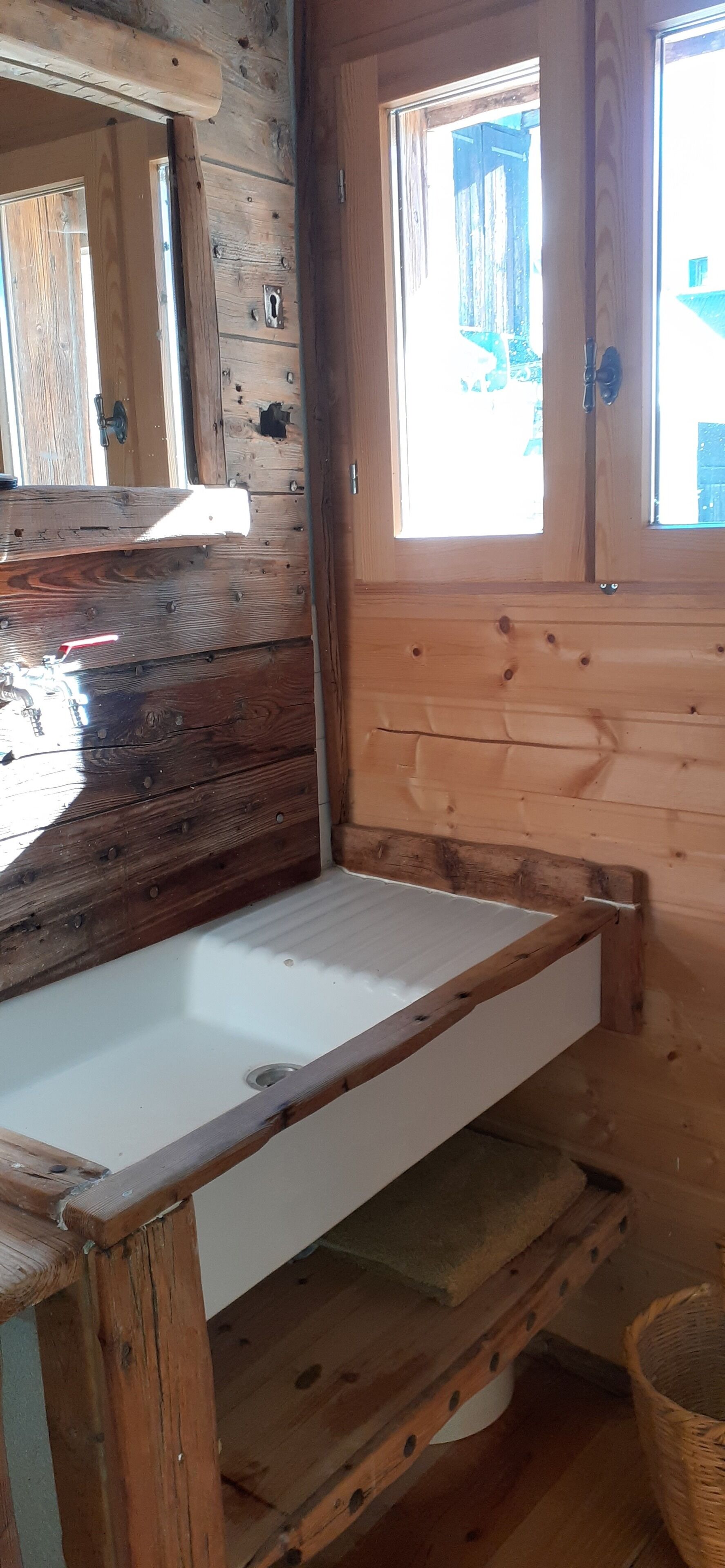 A wooden cabin interior with a white sink, a mirror, and a window.