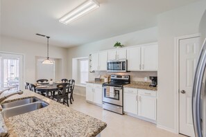 A modern kitchen with white cabinets, granite countertops, stainless steel appliances, and a dining area with a table and chairs.