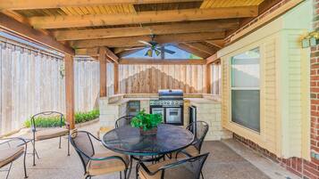 Une terrasse extérieure avec une table ronde, des chaises, un barbecue et un ventilateur de plafond.