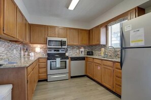 Una cucina con mobili in legno, microonde, piano cottura, lavastoviglie e frigorifero.