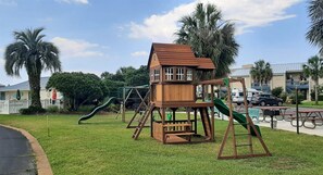 Un’area giochi con una casetta di legno, scivoli e altalene.