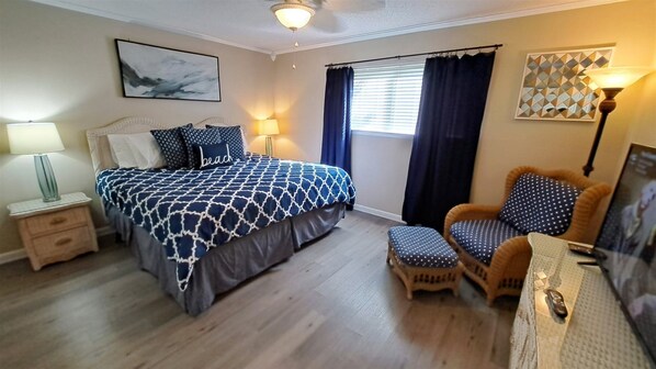 A bedroom with a bed, a chair, a nightstand, a lamp, and a window with curtains.