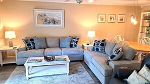 A living room with a grey sectional sofa, two side tables with lamps, a coffee table with books, and a framed picture on the wall.