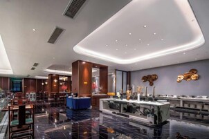 Un vestíbulo de hotel moderno con suelo de mármol, un mostrador de recepción y un área de descanso.