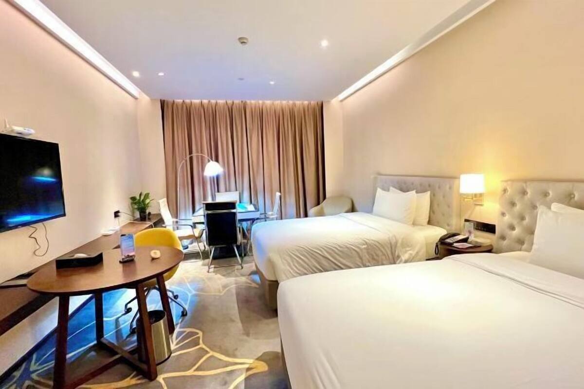 A hotel room with two beds, a desk, a TV, and a lamp.