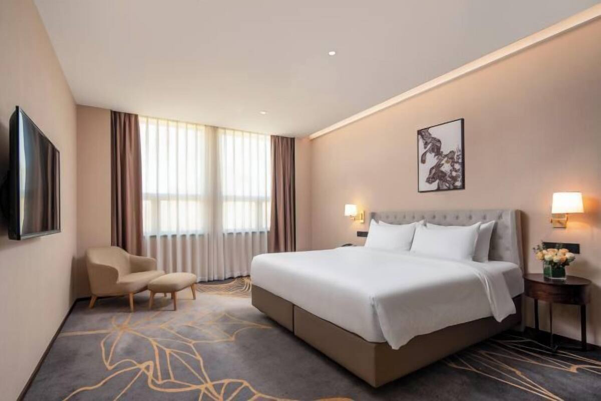 A hotel room with a large bed, a chair, a flat-screen TV, and a painting on the wall.