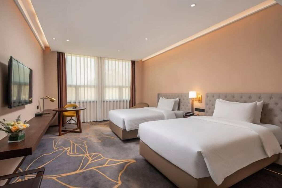 A hotel room with two beds, a desk, a chair, a TV, and a window with curtains.