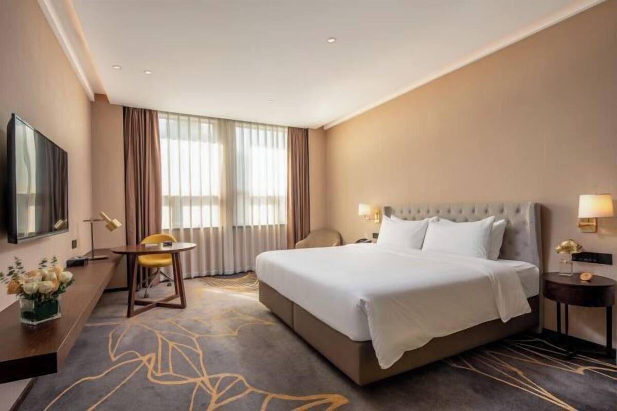 A hotel room with a large bed, a desk with a chair, a TV, and a window with curtains.