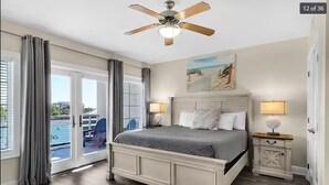 Une chambre avec un grand lit, un ventilateur de plafond, une table de chevet et une vue sur l’extérieur.