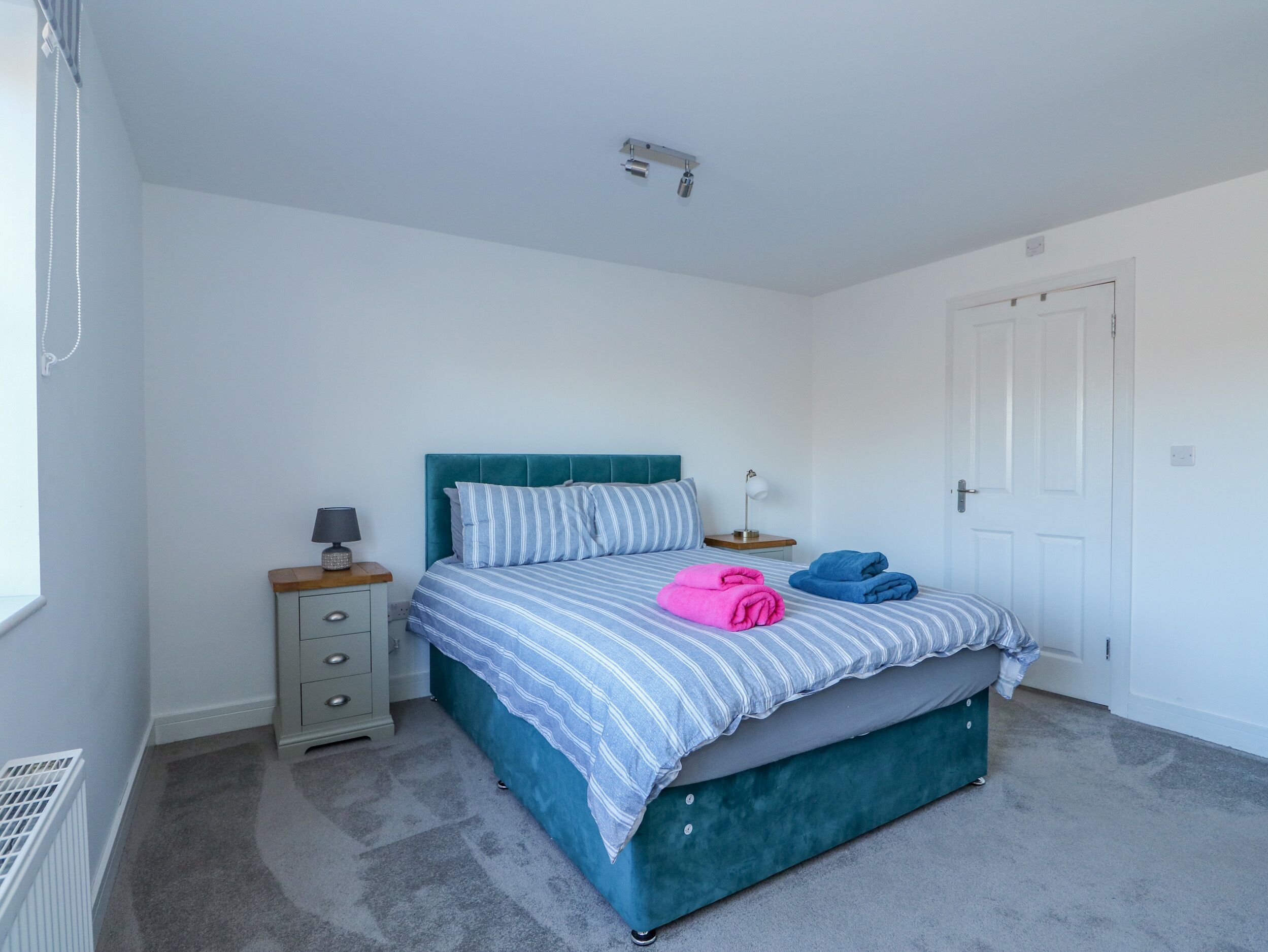 A bedroom with a bed, a nightstand, a drawer unit, and a door.