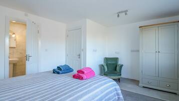 A bedroom with a bed, a wardrobe, a chair, and a bathroom visible through an open door.