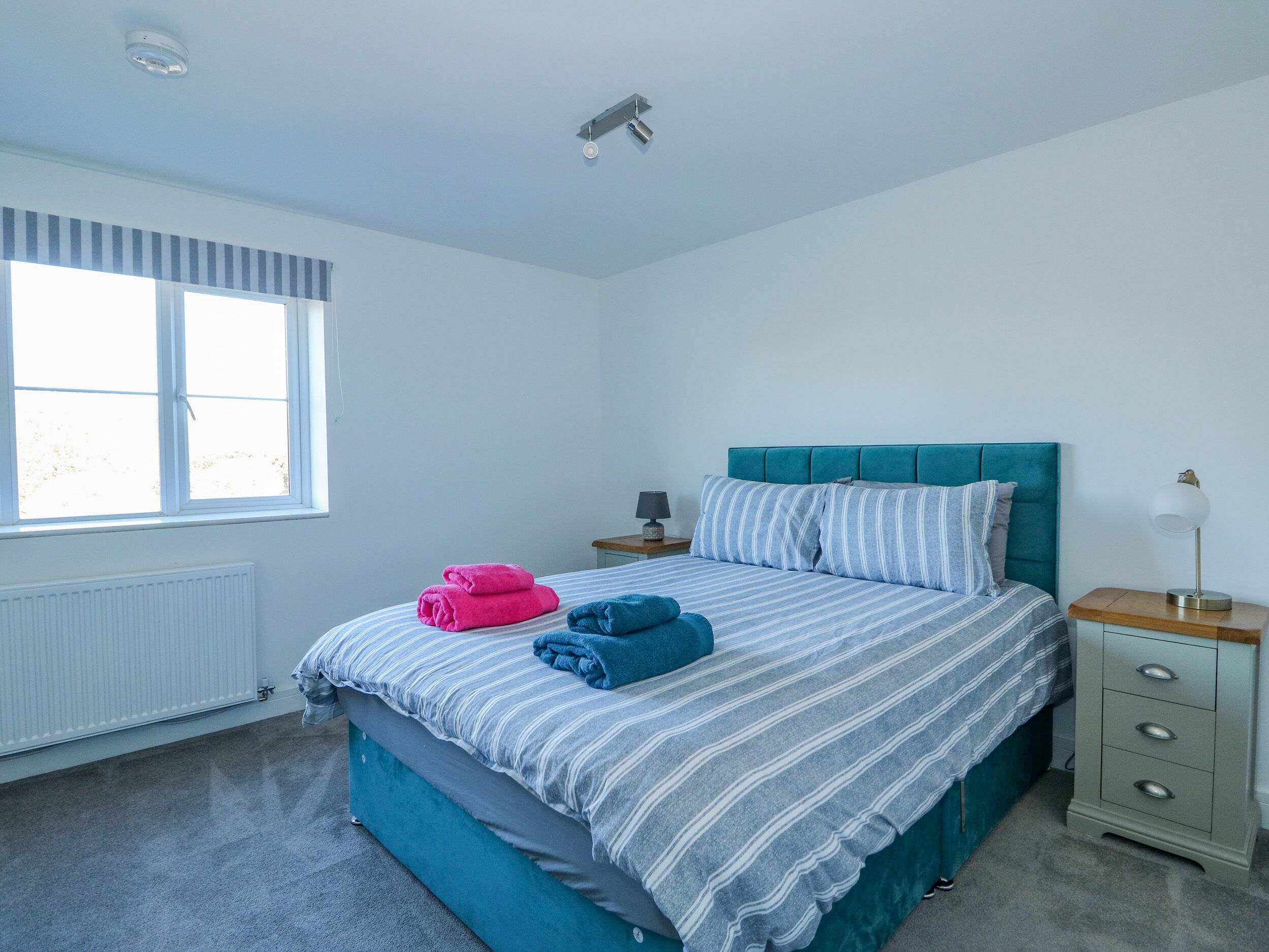 Een slaapkamer met een bed, nachtkastje, lamp en raam.