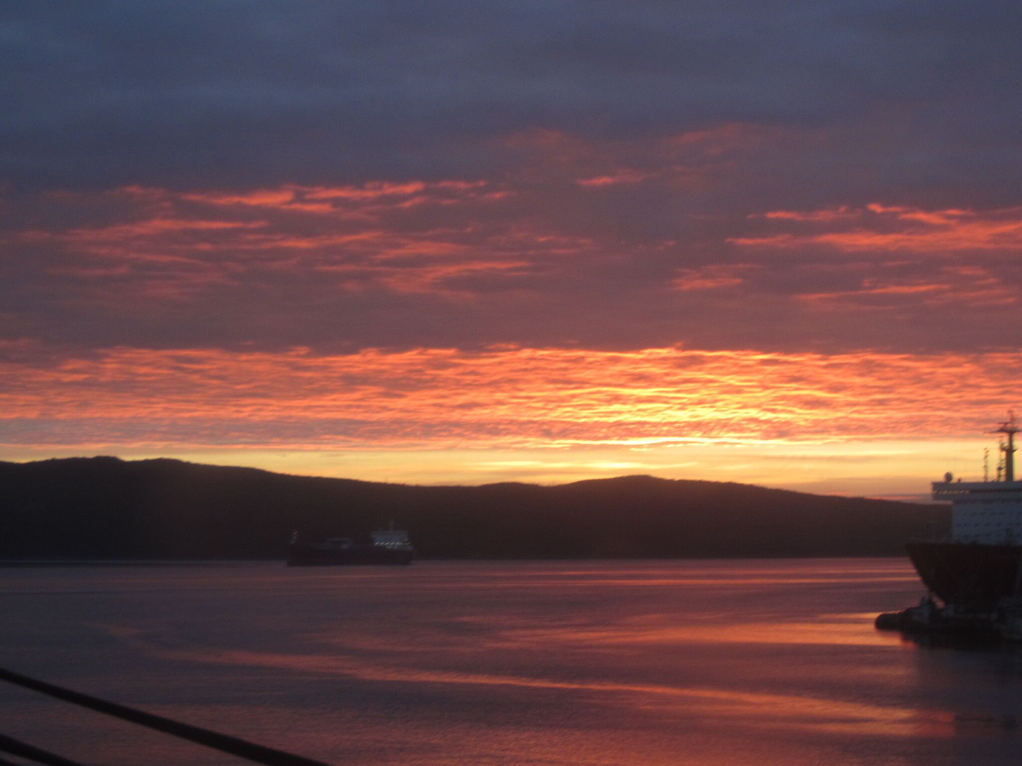 Un atardecer sobre un cuerpo de agua tranquilo con un barco amarrado a la derecha.