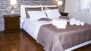 A neatly made bed with a brown bedspread and white linens, two bedside tables with lamps, and a stone-textured wall. - Suestellas, House quiet, relaxing, wifi, eco-friendly, surrounded by greenery (Teulada)