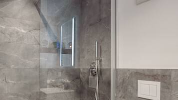 A modern bathroom with a glass-enclosed shower, a white toilet, and marble walls.