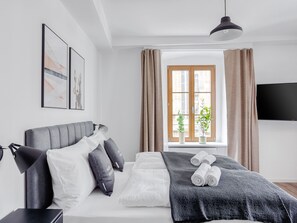 A modern hotel room with a bed, a bedside table, a lamp, a window with curtains, and a flat-screen TV. - Limehome Zwickau Hauptmarkt (Zwickau)