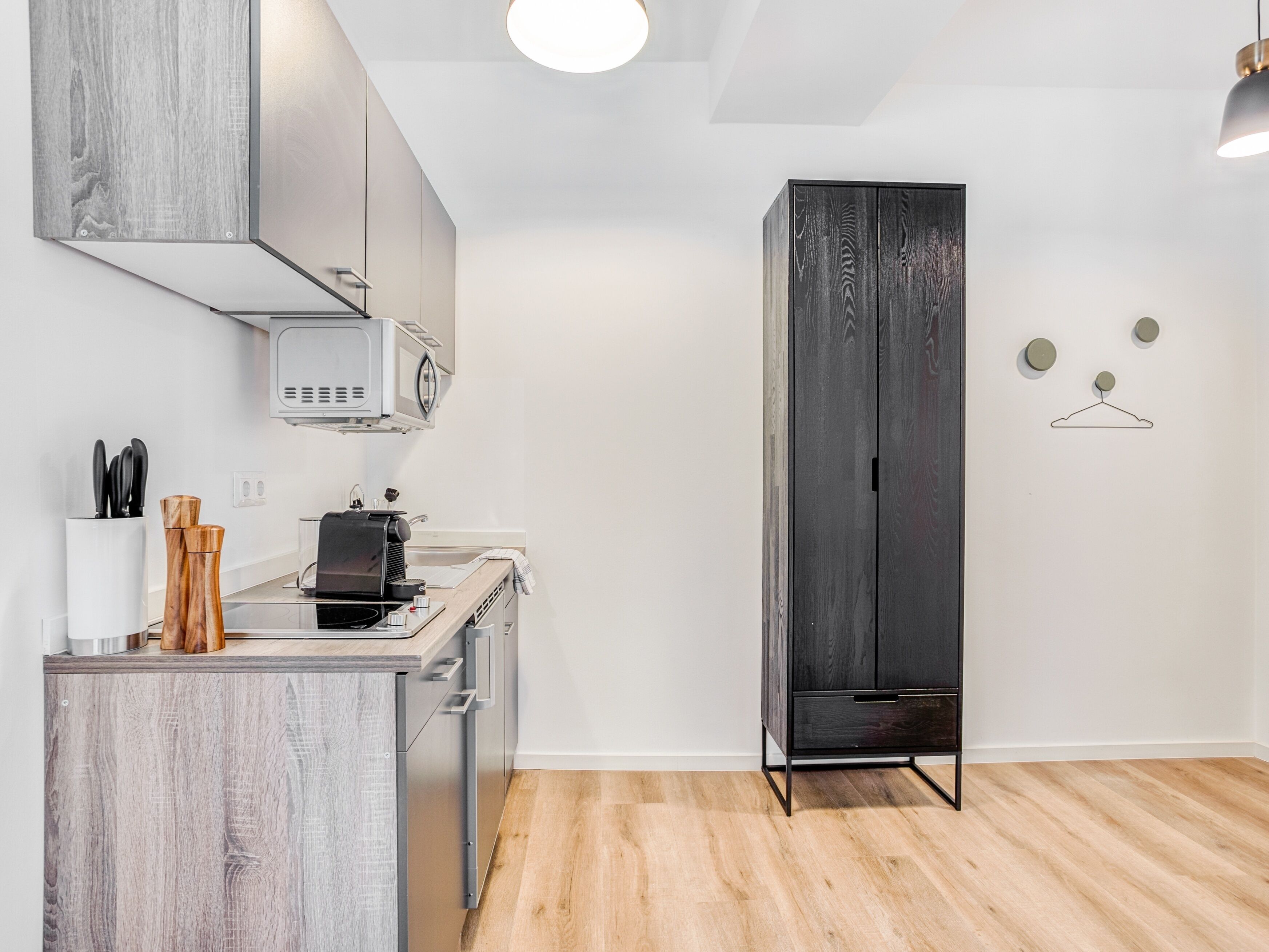 A modern kitchen with a microwave, stove, and cabinets. There is a wooden cabinet and a black wardrobe.