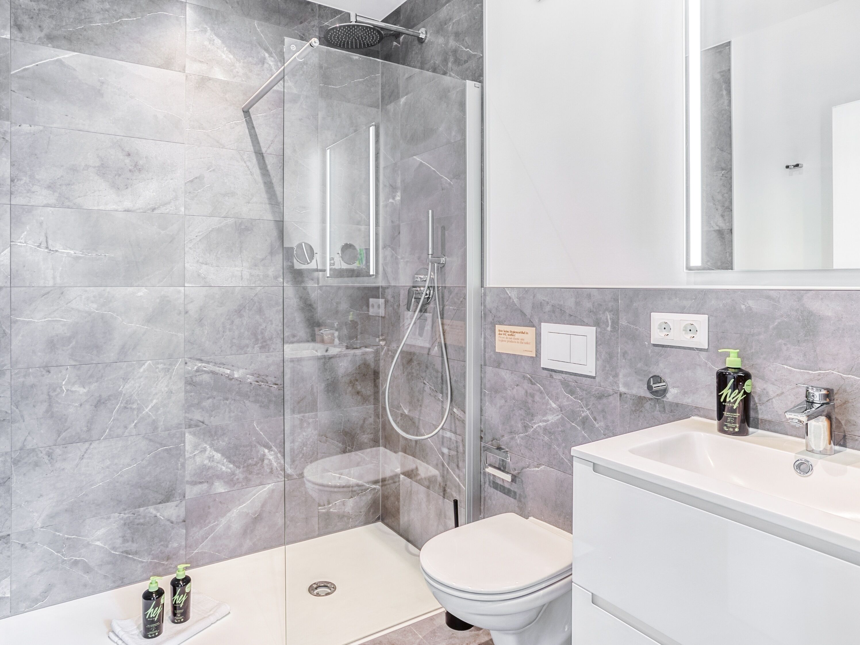 A modern bathroom with a glass-enclosed shower, a white toilet, and a sink with a mirror above it.