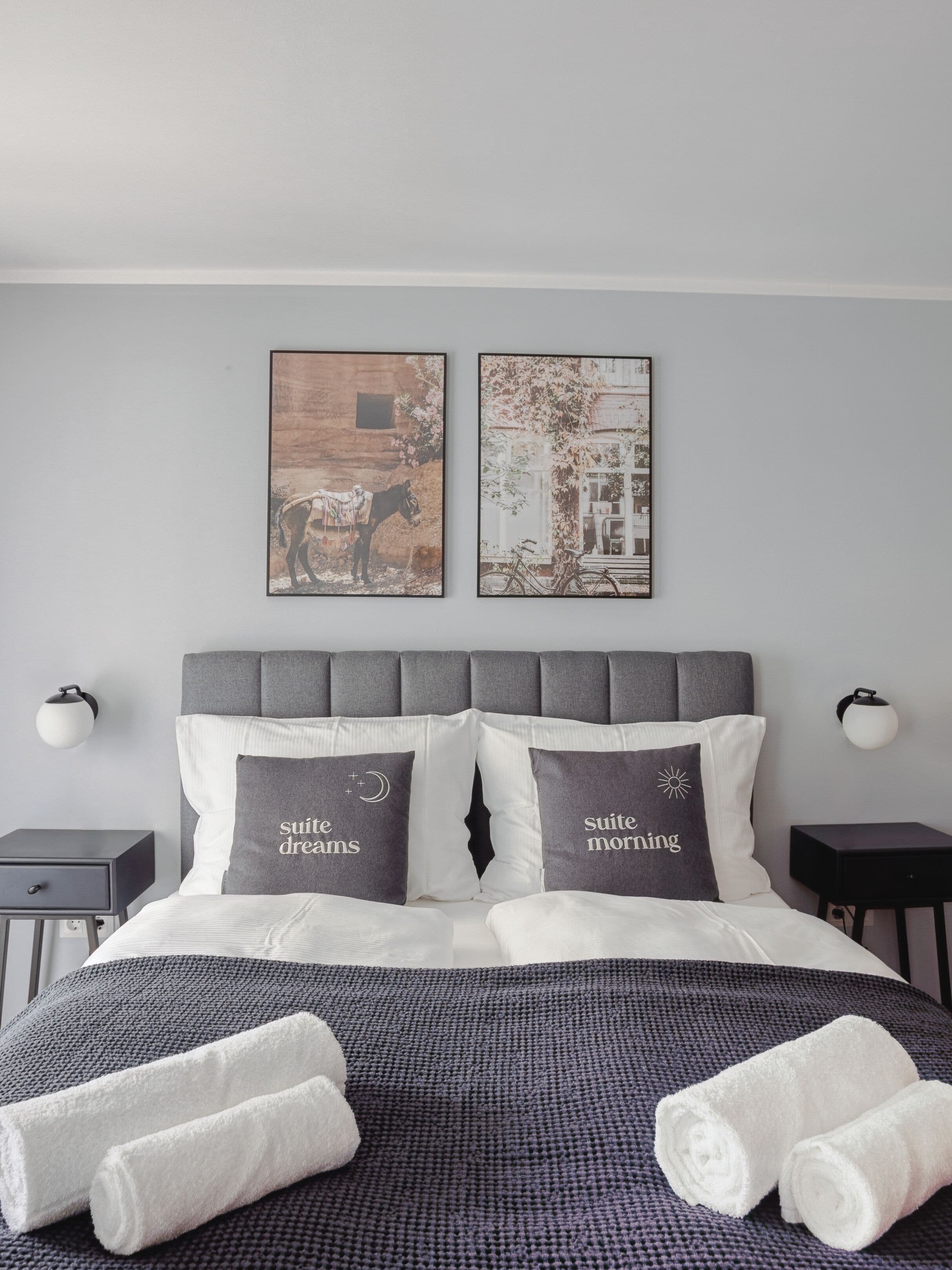 Un lit bien fait, avec deux oreillers, une tête de lit grise et deux lampes fixées au mur.