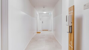 Un couloir lumineux, aux murs blancs, éclairé par un luminaire au plafond, agrémenté d’une pancarte d’accueil et d’un panneau en bois portant un logo.
