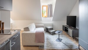 Un espace de vie moderne et bien éclairé, comprenant un canapé, une petite table, un téléviseur et un coin cuisine.