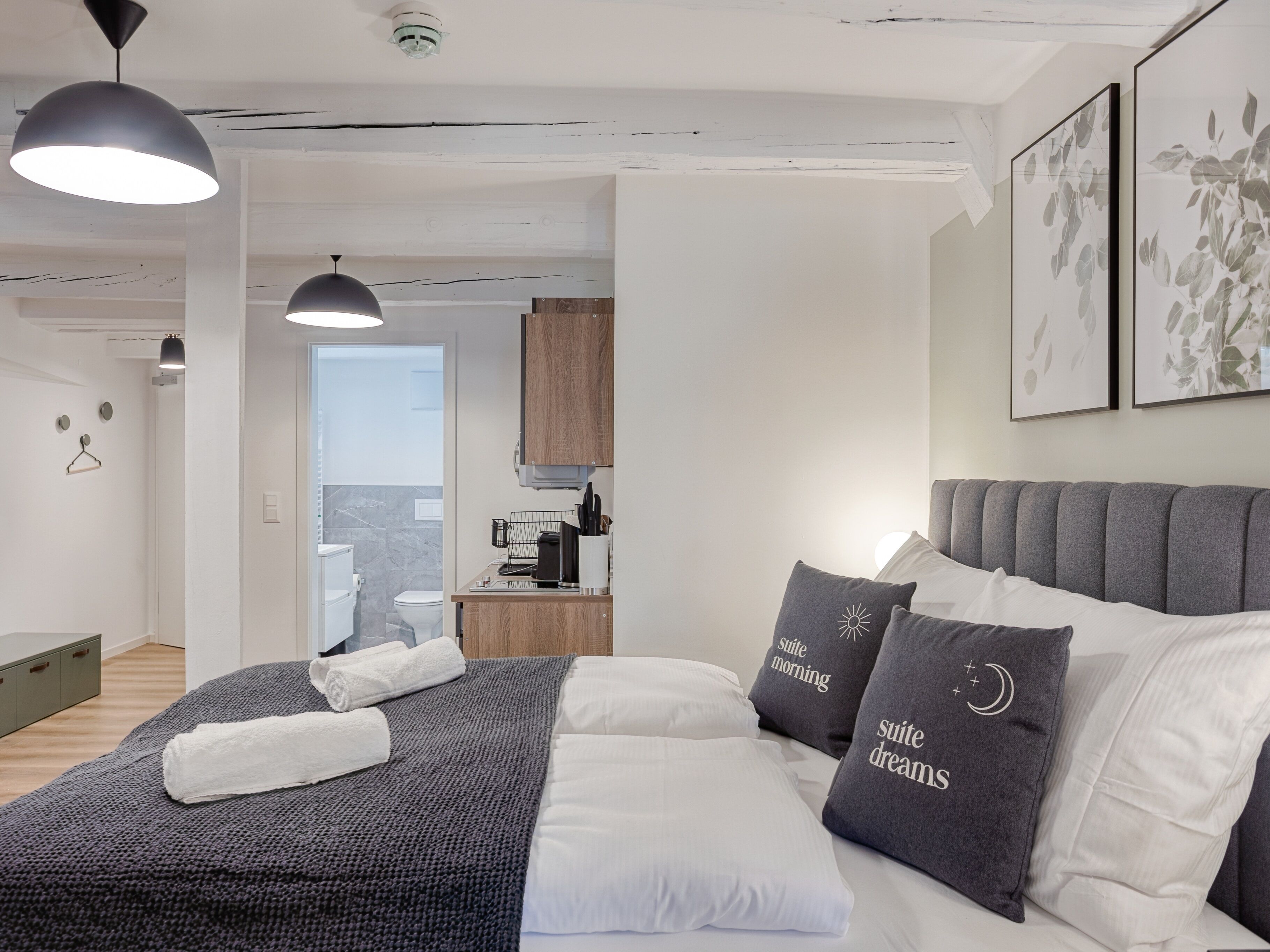 Une chambre moderne avec un grand lit, une literie aux tons de gris et de blanc, et deux lampes de chevet.