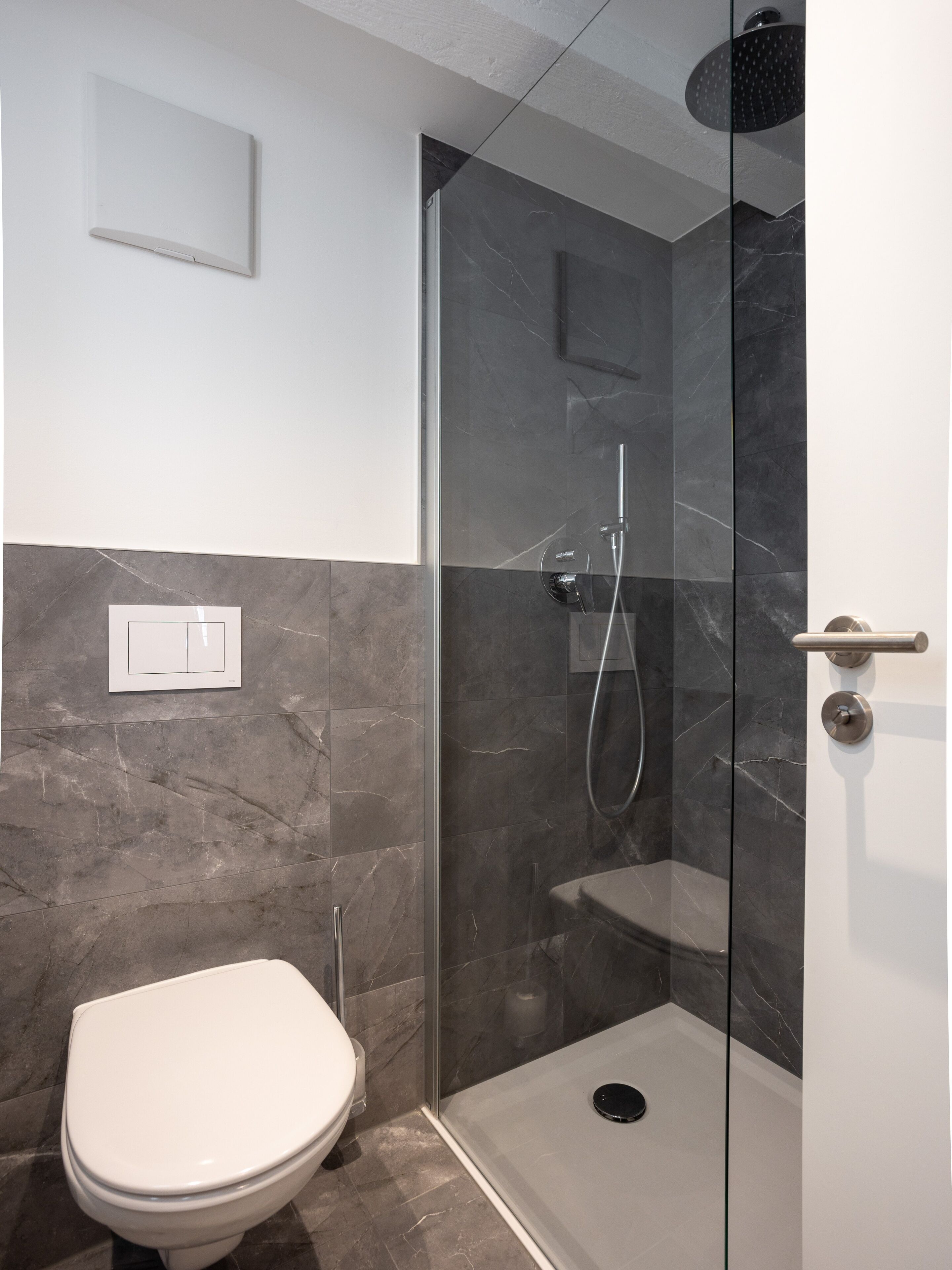 A modern bathroom with a glass-enclosed shower, a toilet, and a marble-tiled wall.
