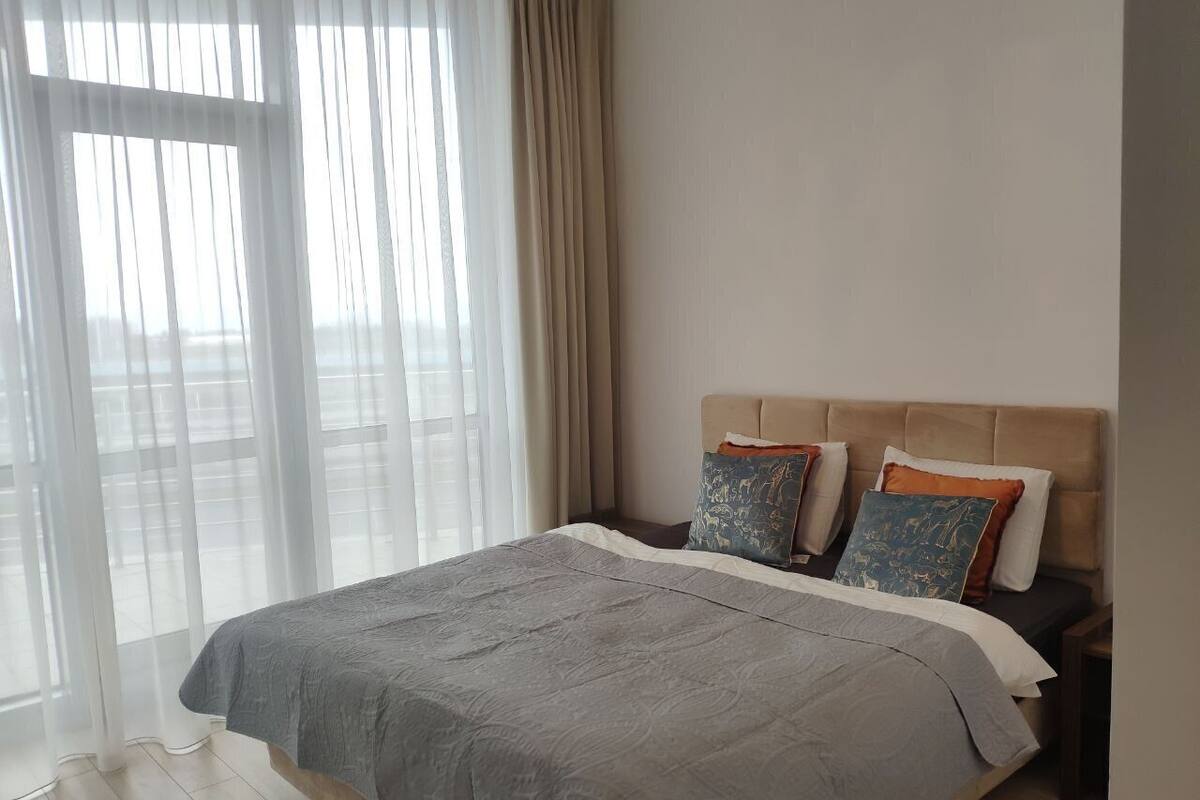 A bedroom with a large bed, a headboard, and a window with sheer curtains.