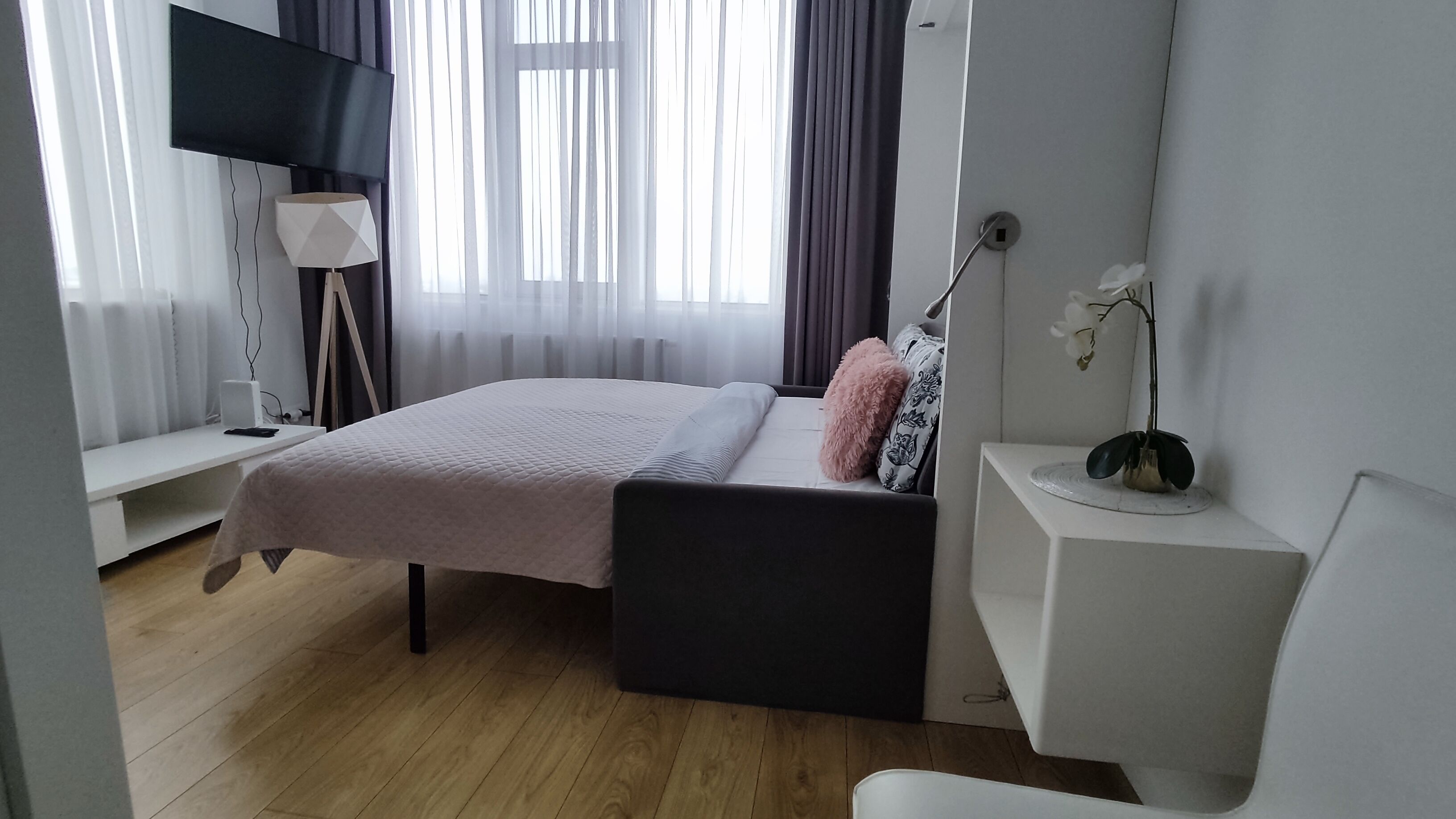 Un dormitorio moderno con cama, mesita de noche, lámpara y un pequeño escritorio.