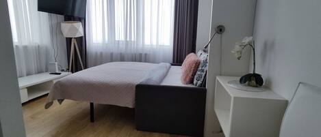 Un dormitorio moderno con cama, mesita de noche, lámpara y un pequeño escritorio.