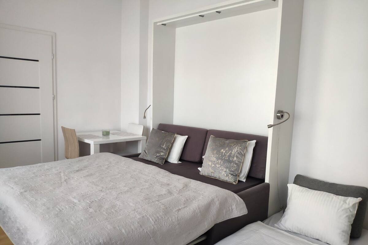 A modern bedroom with a large bed, a smaller bed, a desk, and a chair.