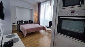 A modern hotel room with a bed, a desk with a computer, a flat-screen TV, and a built-in oven. - Apartamenty Varsovia 304 (Warsaw)