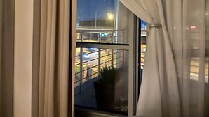 A room with a large window, curtains, a bed, and a view of an outdoor area with lights. - Apartamenty Varsovia 304 (Warsaw)