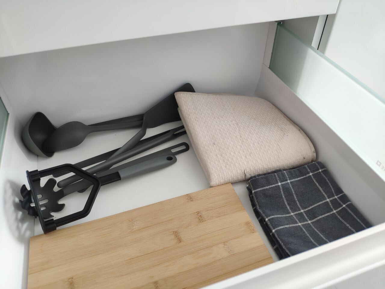 A neatly organized storage space with a cutting board, a black spatula, a beige cushion, and a plaid cloth.