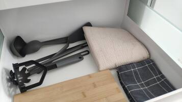 Un espacio de almacenamiento ordenado con una tabla de cortar, una espátula negra, un cojín color beige y un paño escocés.