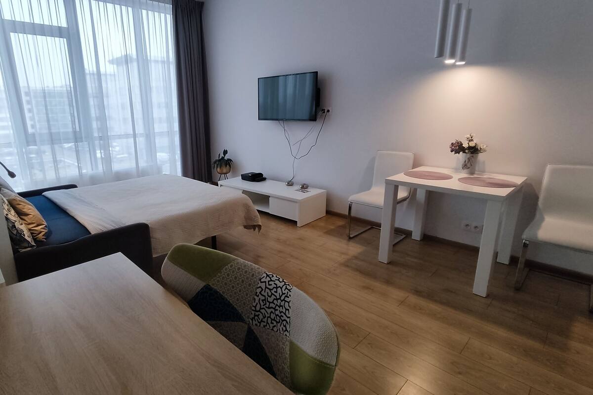 A hotel room with two beds, a desk, a chair, a TV, and a small table with a vase of flowers.