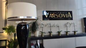 A reception area with a modern lamp, a sign reading "VARSOVIA JEROZOLIMSKIE", and several potted plants. - Apartamenty Varsovia 304 (Warsaw)
