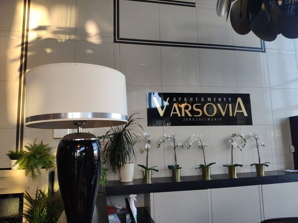 A reception area with a modern lamp, a sign reading "VARSOVIA JEROZOLIMSKIE", and several potted plants. - Apartamenty Varsovia 304 (Warsaw)