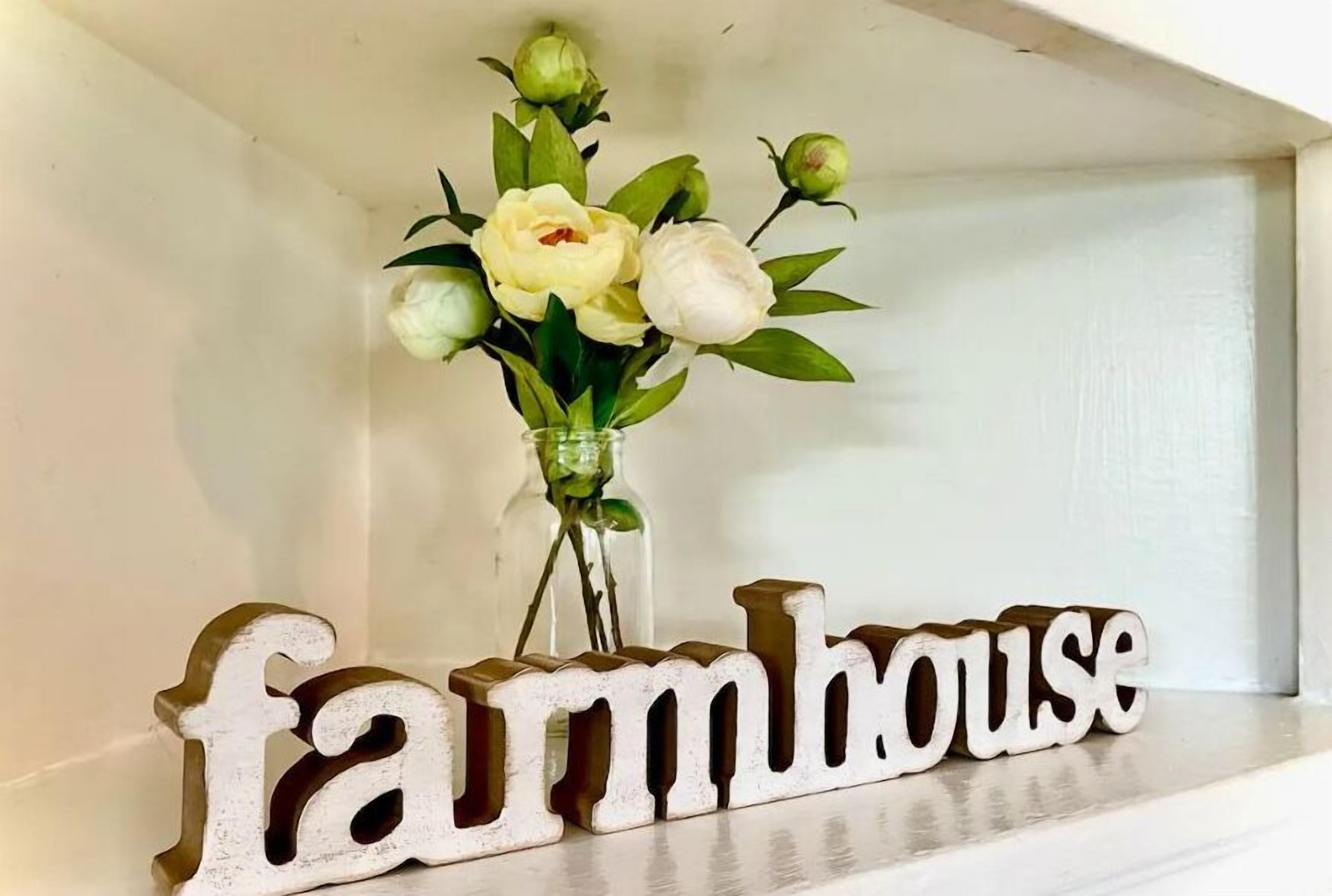 A shelf with a vase of flowers and wooden letters spelling "farmhouse".