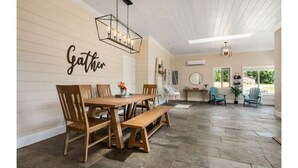 A dining area with a wooden table and chairs, a bench, and a wall-mounted sign that reads "Gather". - Charming 2BR Farmhouse Amazing View of Mt. Rainier - Family Friendly + Game Barn (Mineral)
