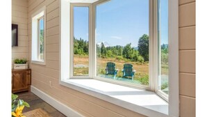 A room with a large bay window overlooking a grassy area with two Adirondack chairs. - Charming 2BR Farmhouse Amazing View of Mt. Rainier - Family Friendly + Game Barn (Mineral)